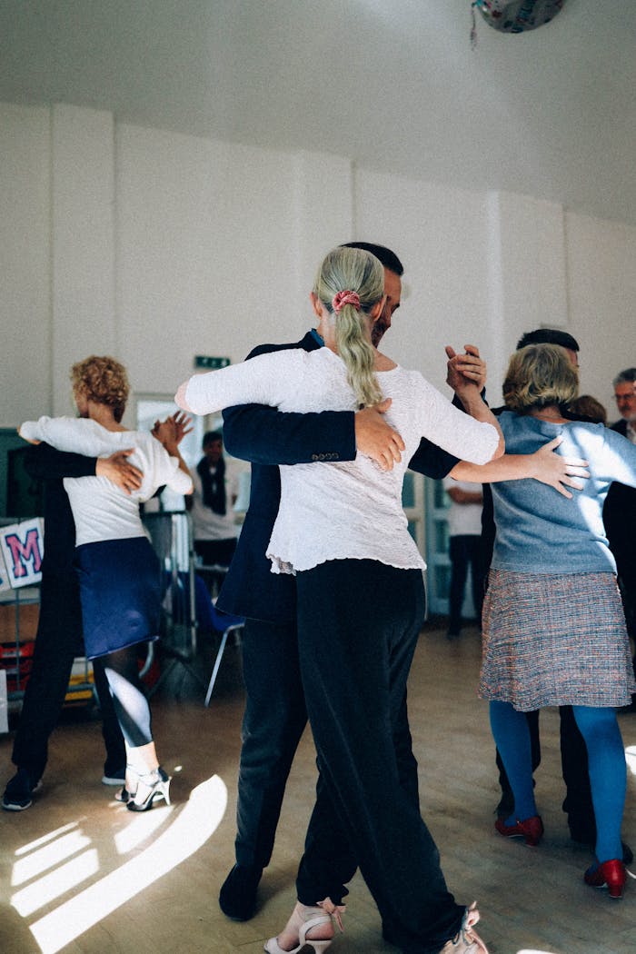 A group of adults practicing ballroom dancing in a sunlit indoor studio, capturing elegance and grace.