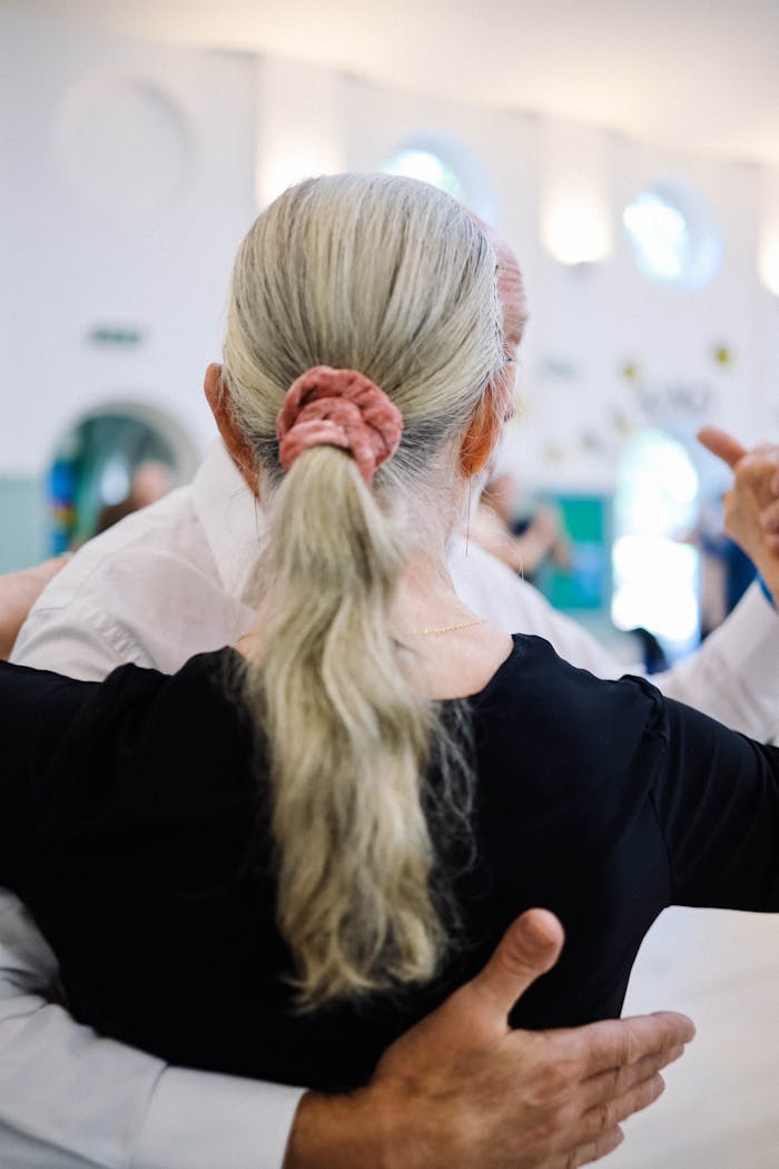 Elderly couple embraces while dancing tango in a bright ballroom setting.