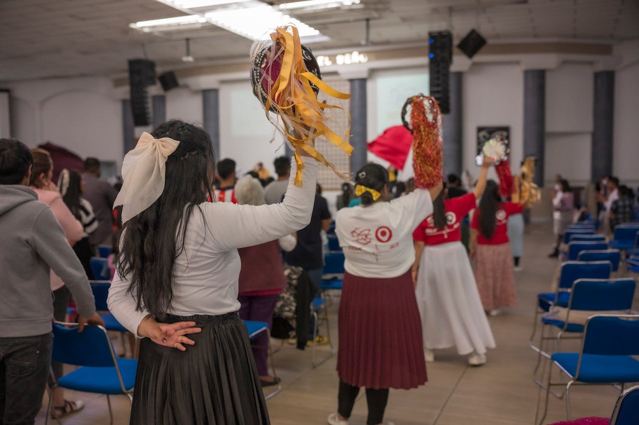 People engaged in a lively cultural dance in a community hall, raising colorful pom-poms.