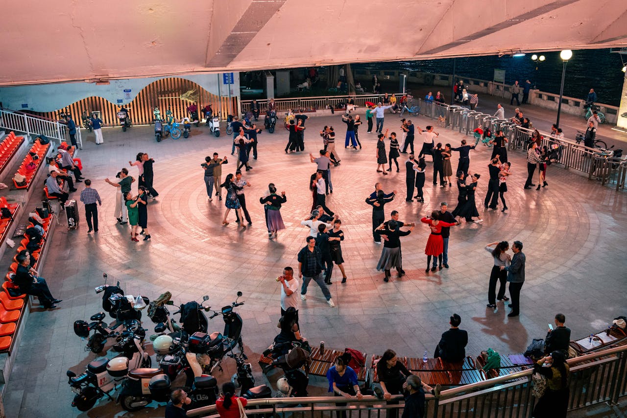 Group of people enjoying an evening dance at an outdoor urban plaza under bright lights.